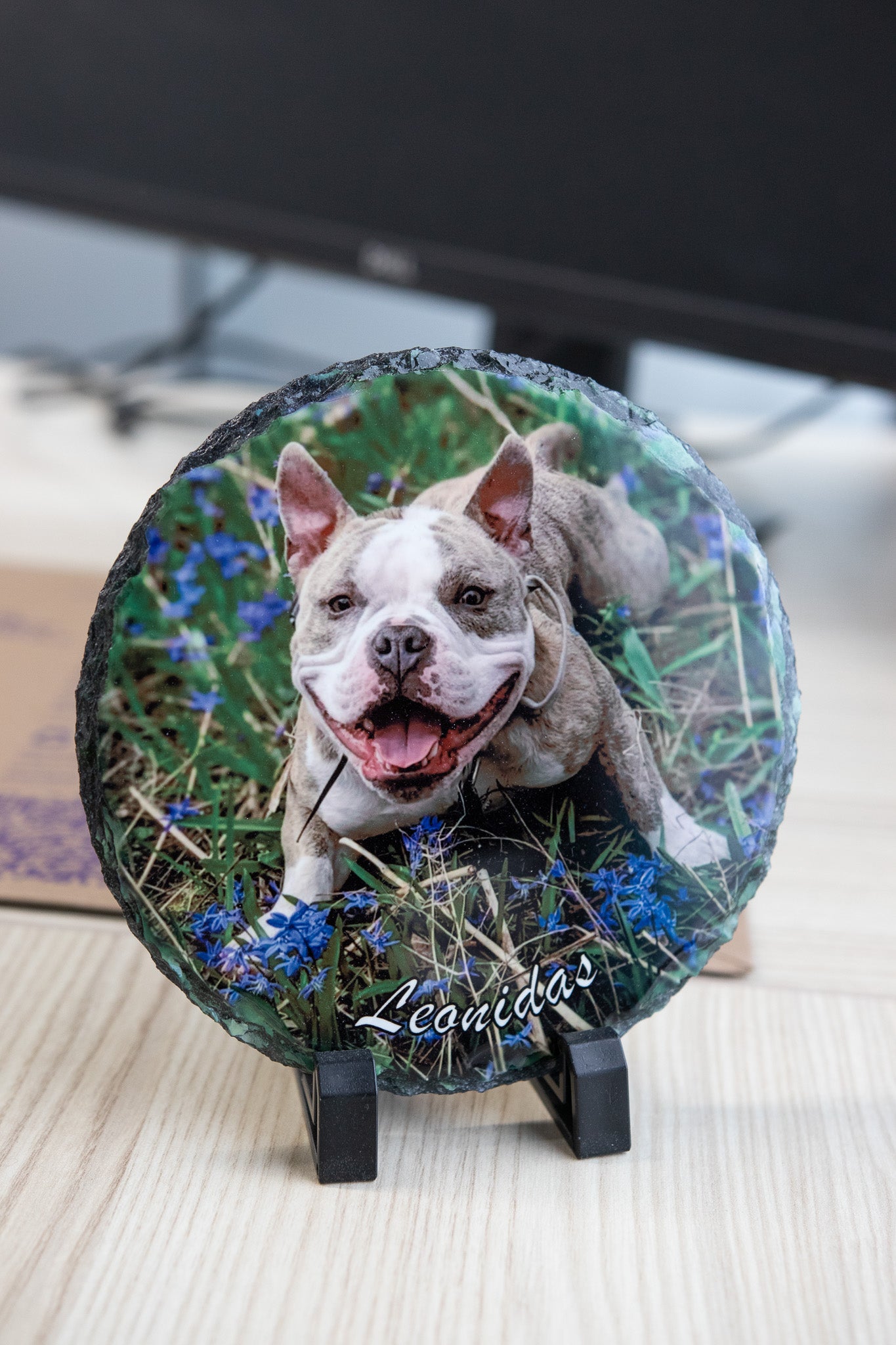 Round slate with a dog photo and 'Leonidas' text on a stand sitting on desk