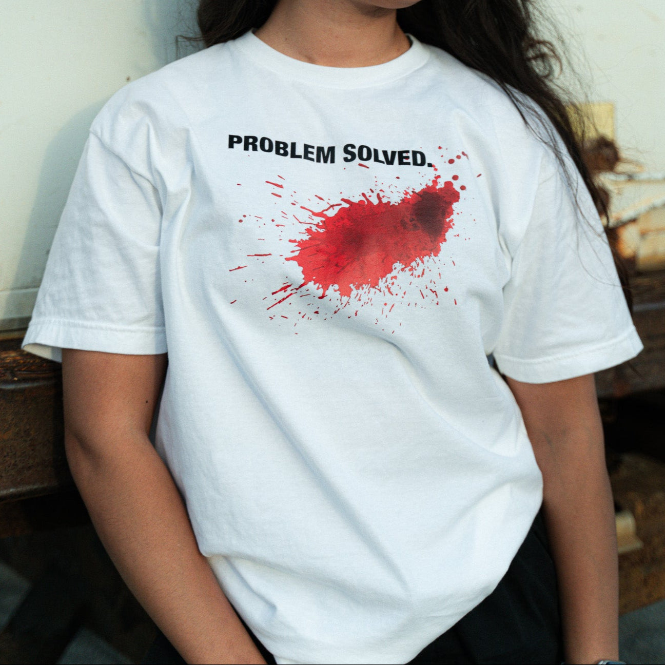 Person wearing a white t-shirt with a red splatter design and text against a white wall.