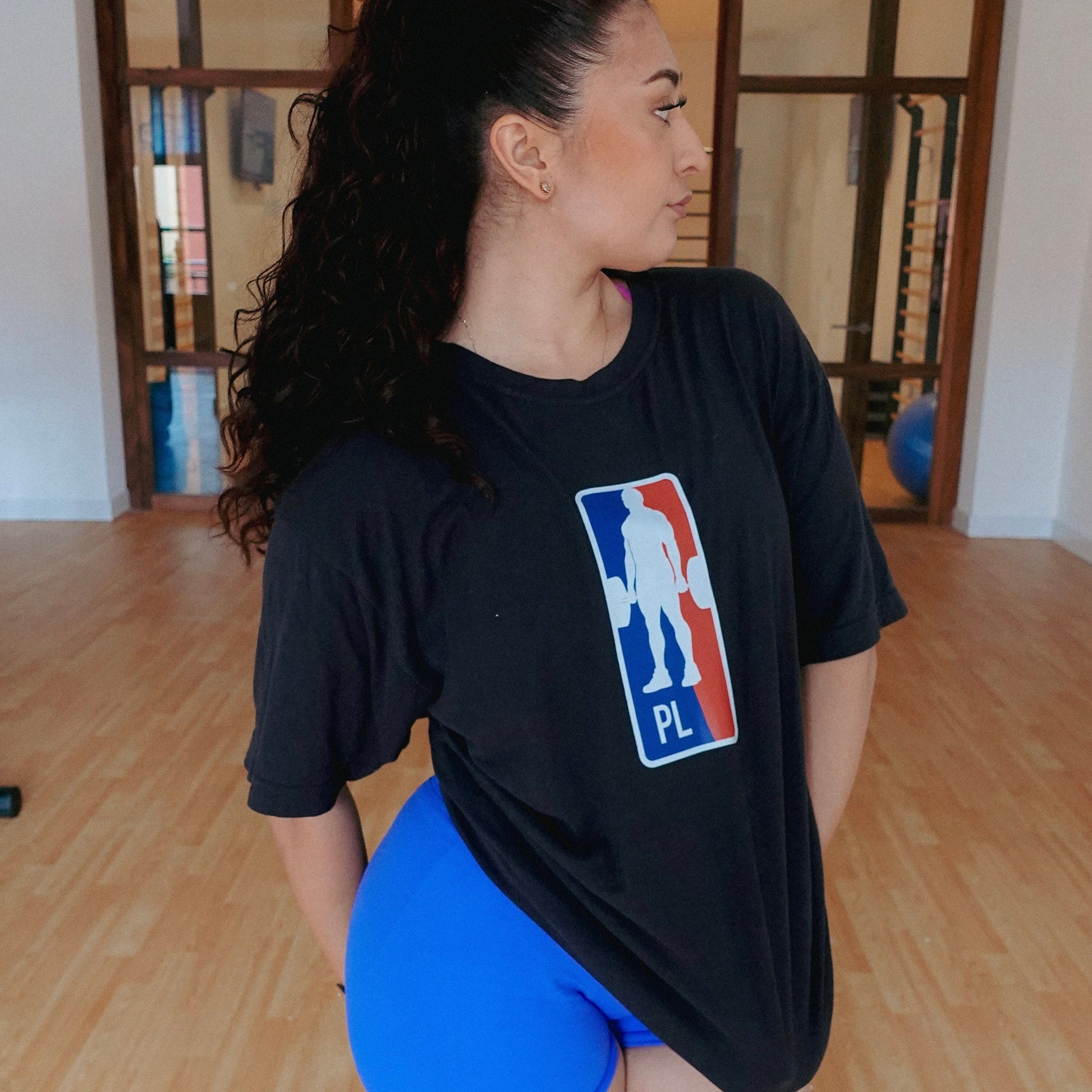 Woman wearing a black t-shirt with a logo and blue shorts in an indoor setting
