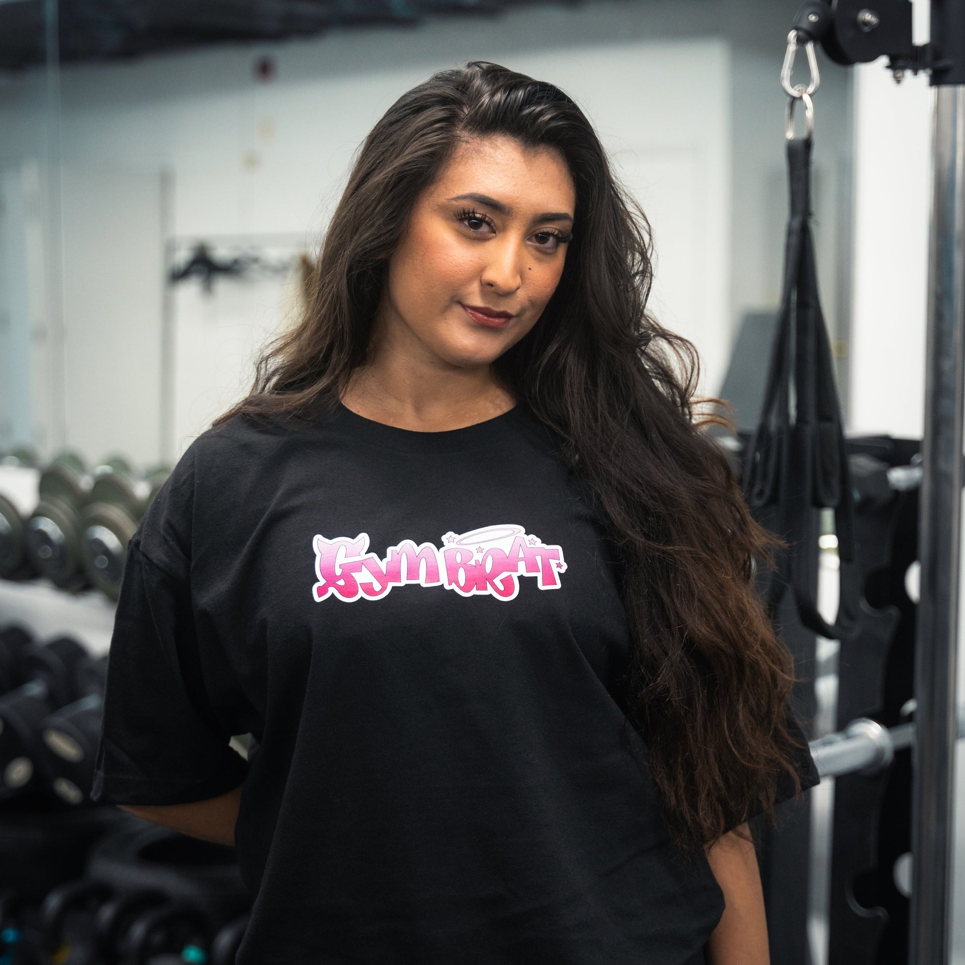 Woman wearing a black t-shirt with pink and white text in a gym setting gym brat tee y2k