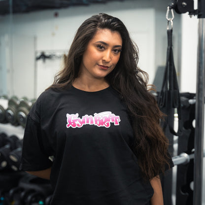 Woman wearing a black t-shirt with pink and white text in a gym setting gym brat tee y2k