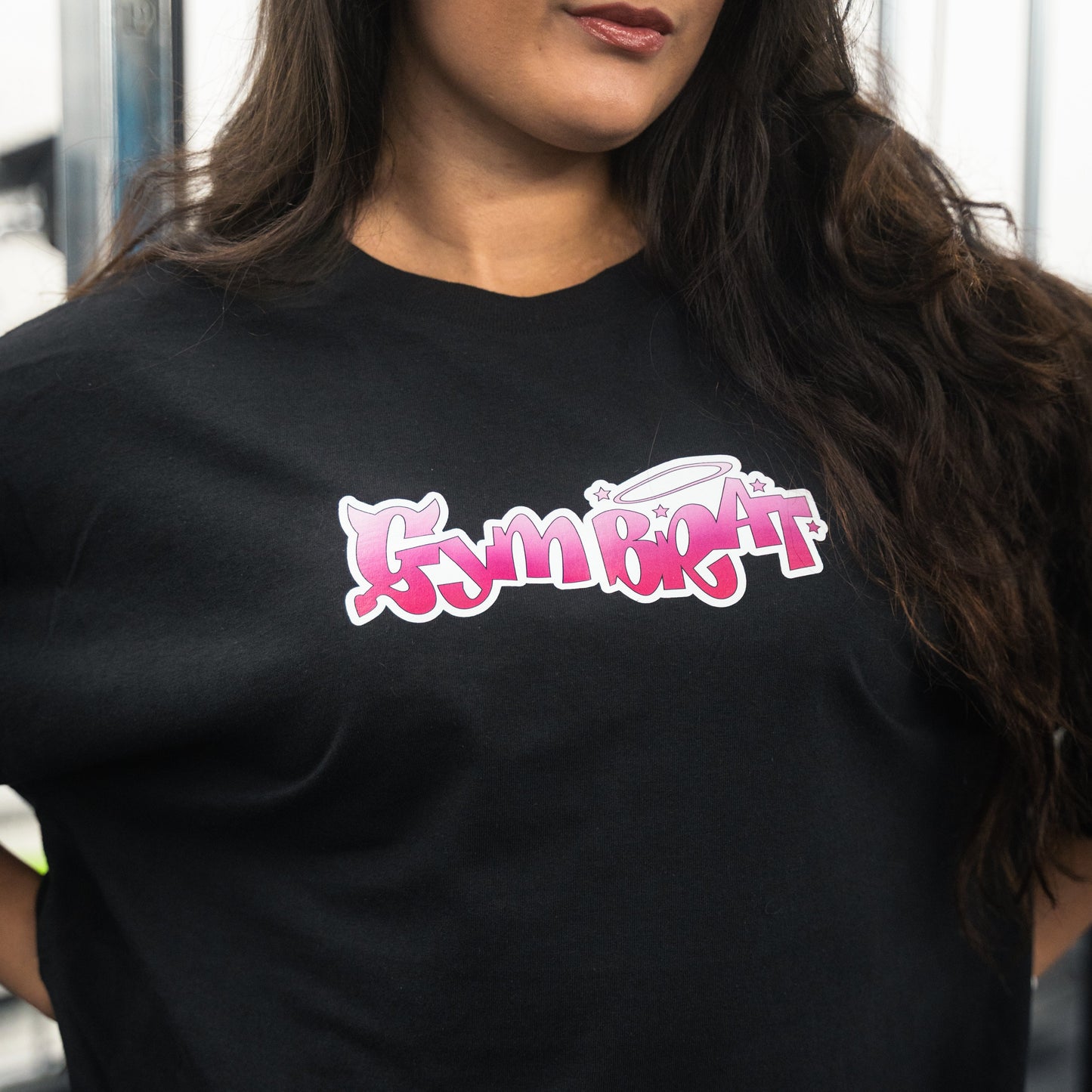 Person wearing a black t-shirt with pink and white text design. gym brat tee y2k