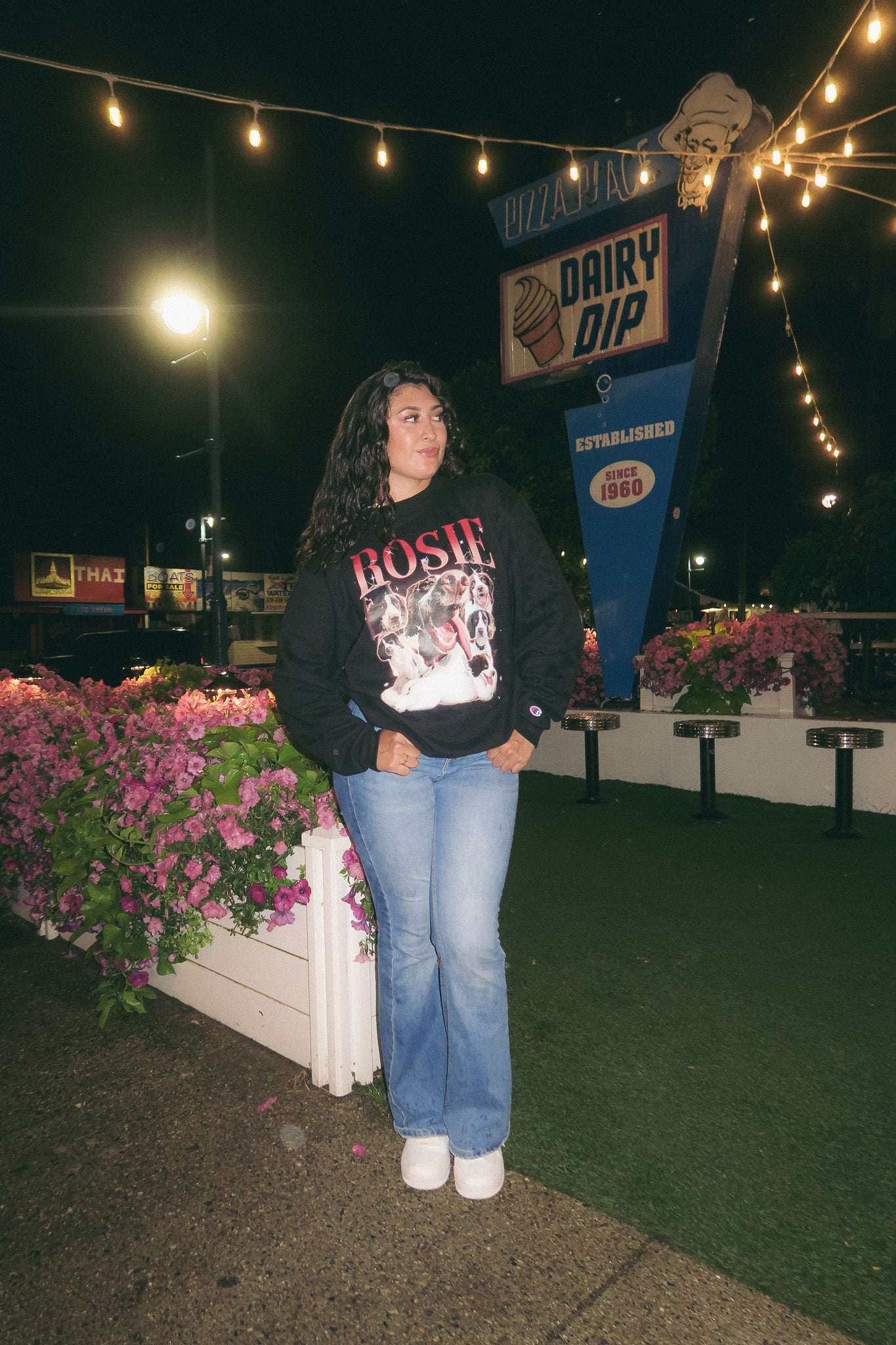 Person standing in front of a Dairy Dip sign at night with decorative lights and flowers. Custom Retro Crewneck Vintage
